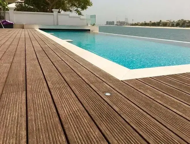 μια κατασκευή από καφέ wpc deck, συνθετικό ξύλο, που χρησιμοποιείται για να περπατάμε γύρω από την πισίνα με τα γαλαζοπράσινα νερά